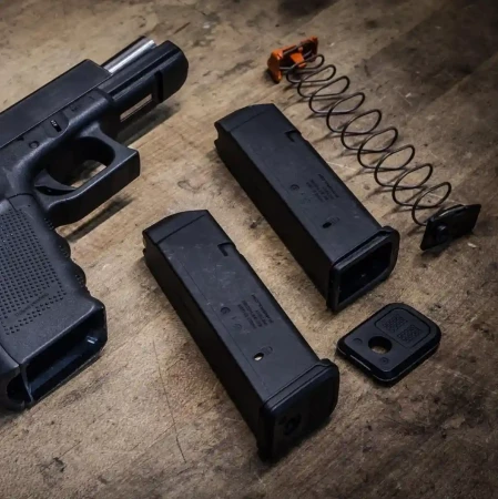 Dwa magazynki Magpul Pmag 17 GL9 leżą obok pistoletu Glock 17. Jeden z nich jest rozłożony.