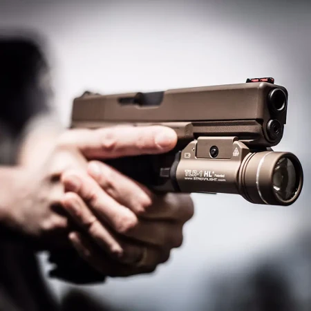 Latarka pistoletowa Streamlight TLR-1 HL FDE na pistolecie Glock trzymanym w dłoniach strzelca.