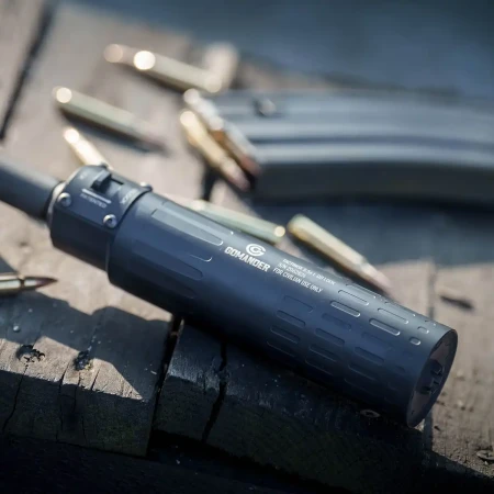 Tłumik Gomander TACTINOX QD-LOCK L 5.56 mm na stole obok magazynka z amunicją.